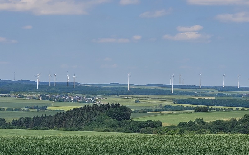 Weiter Blick über eine Mittelgebirgslandschaft, am Horizont stehen Windräder