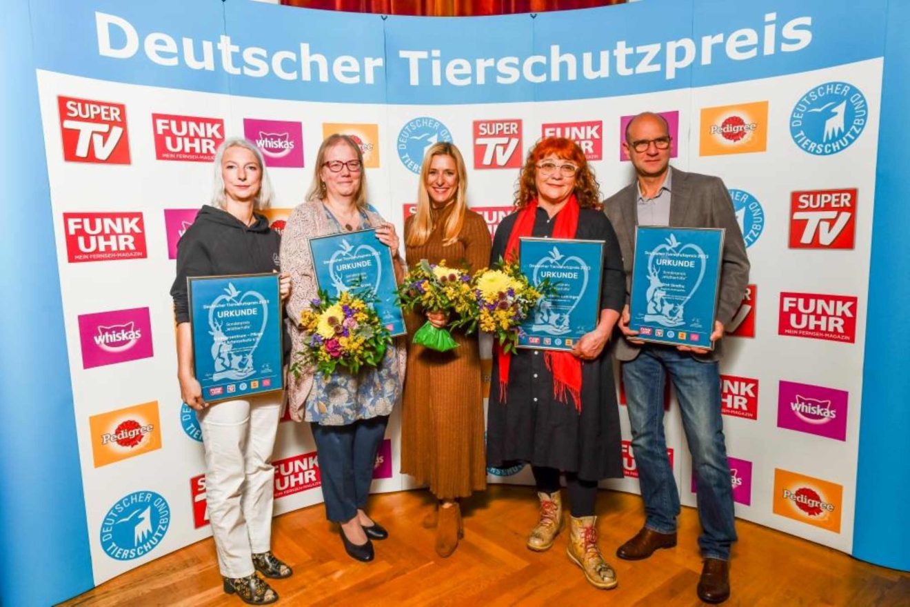 Fünf Personen mit Urkunden und Blumensträußen stehen vor einem Plakat mit dem Text "Deutscher Tierschutzpreis" und vielen Sponsorenlogos