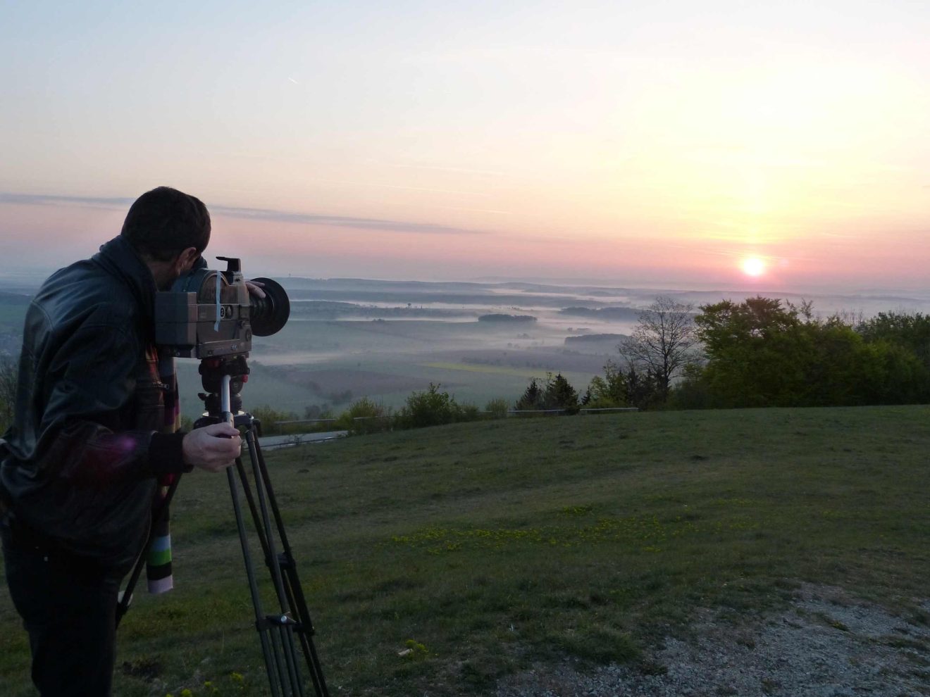 Ein Mann schaut durch eine Filmkamera auf eine Landschaft im Sonnenaufgang