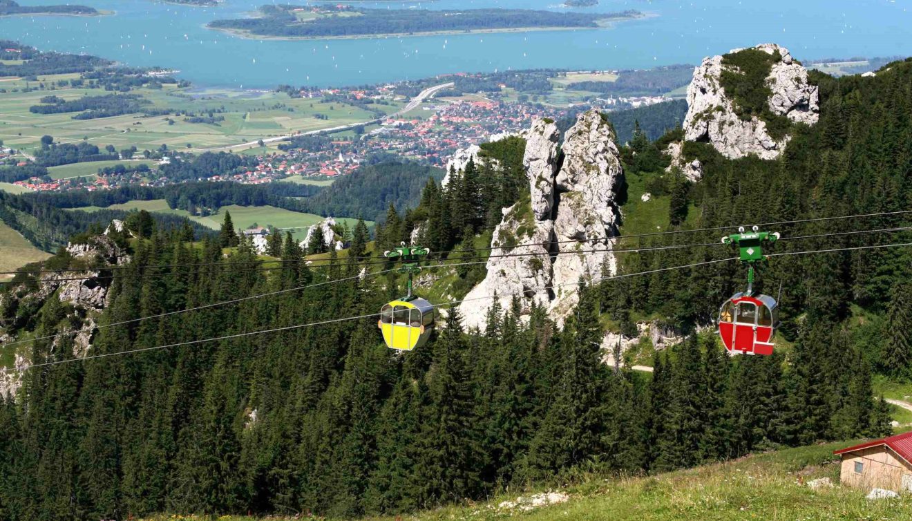 Vor der Kulisse des Chiemsee ziehen eine rote und eine gelbe Berggondel den Berg hinauf
