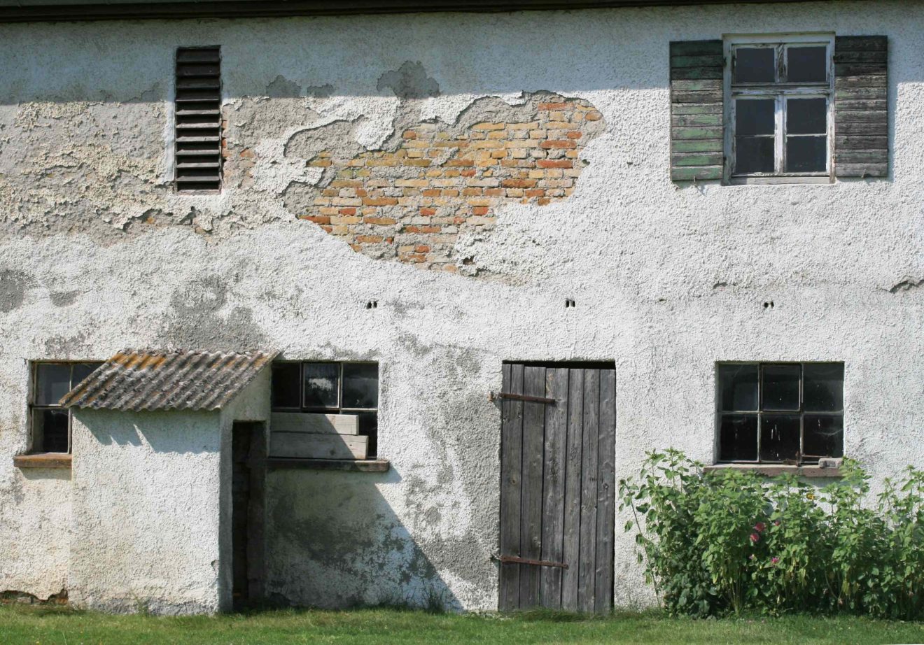 Blick auf eine alte Gemäuerwand mit Holztüren und alten Fenstern