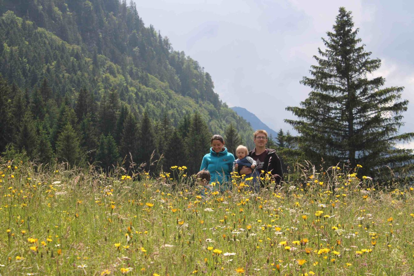 In einer blühenden Bergwiese steht eine junge Familie