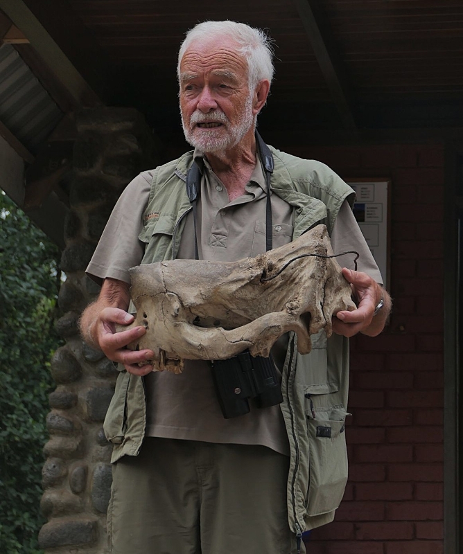 Ein weißbärtiger Mann in khaki-Kleidung hält einen Tierschädel in der Hand