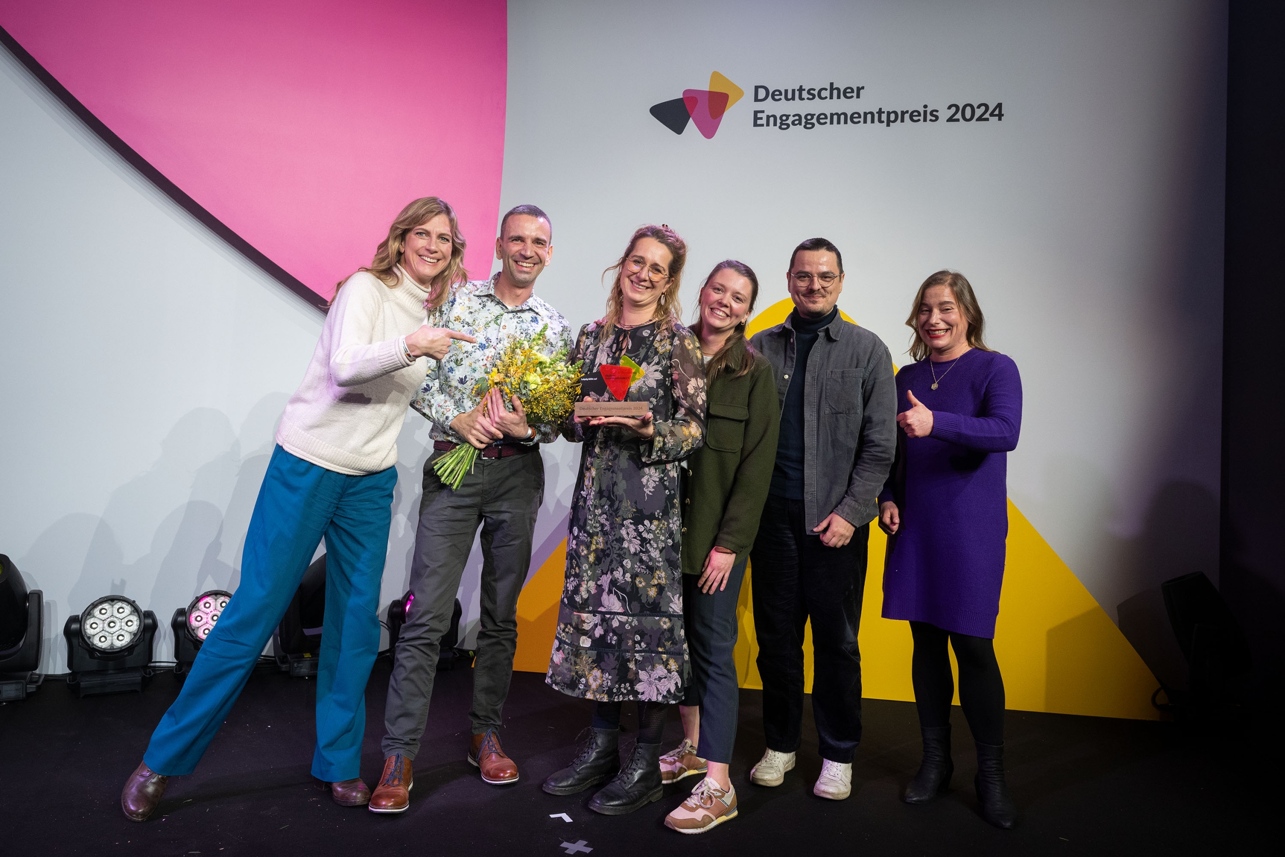Eine Gruppe Menschen, teils mit Blumensträußen in der Hand, posiert vor einer Logowand des Deutschen Umweltpreises