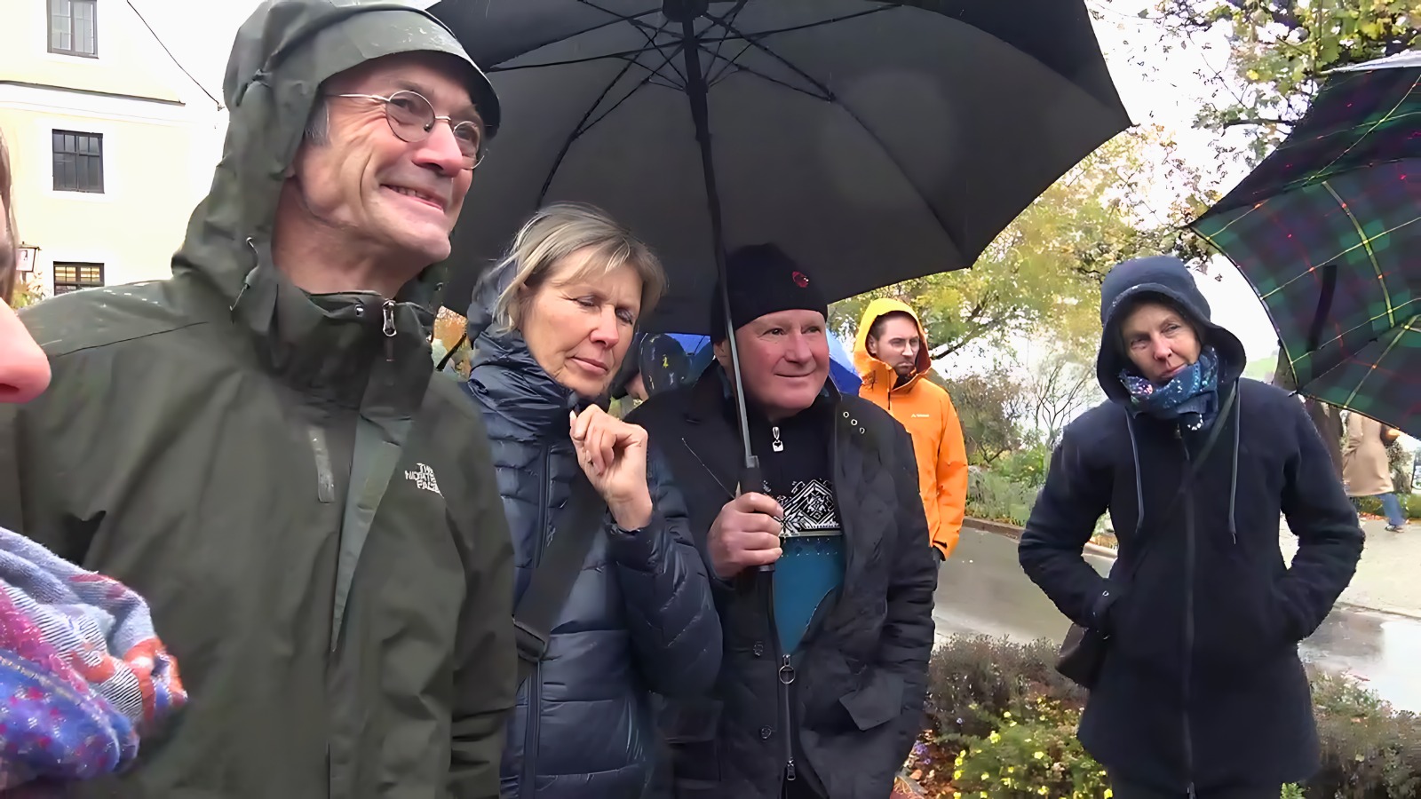 Einige Personen in Regenkleidung und unter Schirmen