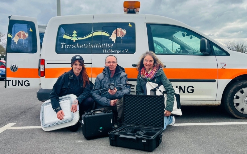 Vor einem Kastenwagen mit signalfarbenem Streifen sitzen drei Menschen mit Equipment für die Wildtierrettung