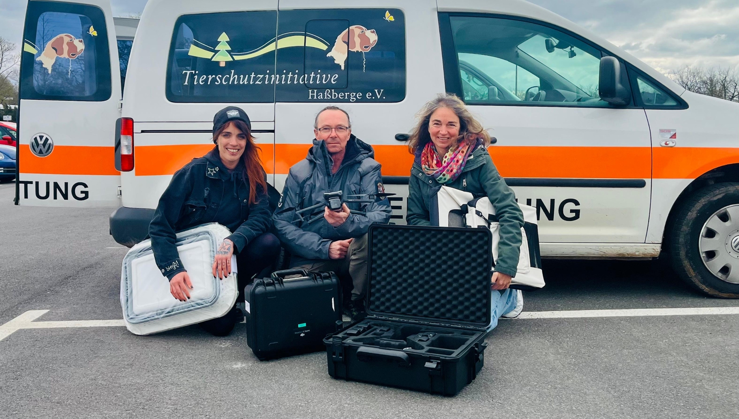 Vor einem Kastenwagen mit signalfarbenem Streifen sitzen drei Menschen mit Equipment für die Wildtierrettung