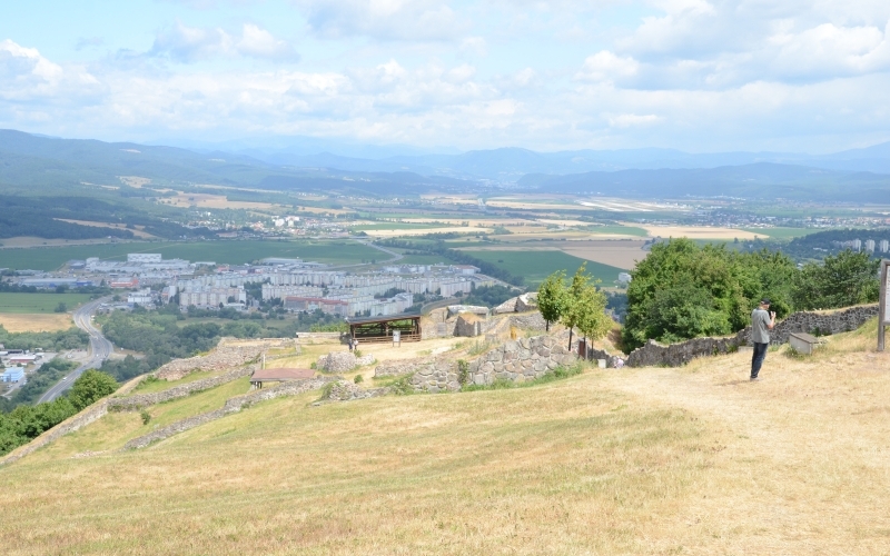 Blick über eine Landschaft mit Stadtteil von einem kahlen Bergrücken, auf dem Ruinenteile zu sehen sind und ein Mensch fotografiert.