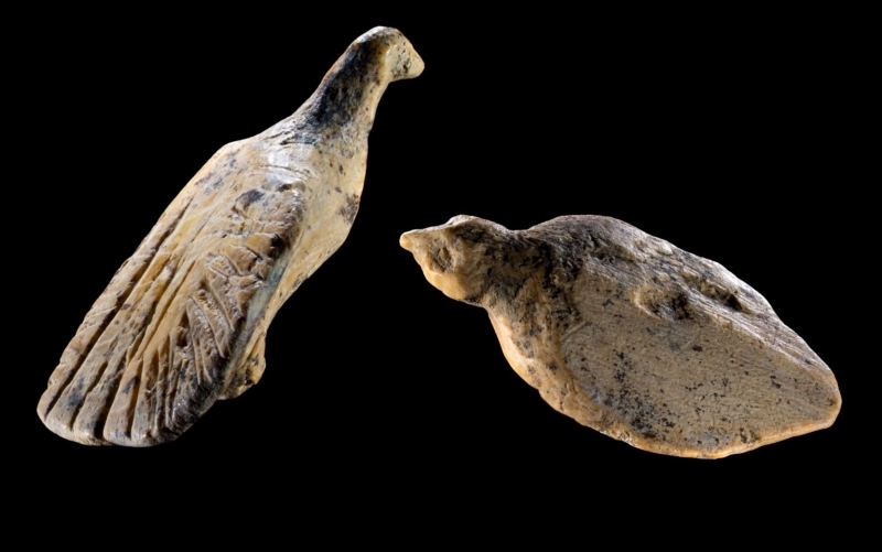Vor schwarzem Hintergrund zwei geschnitzte Vogelfiguren