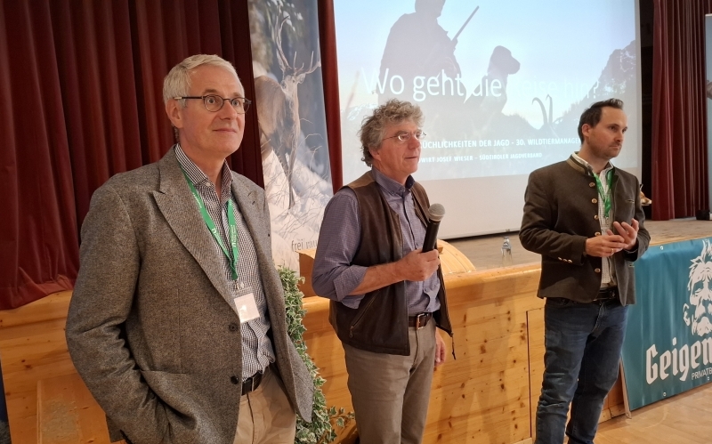 Drei Männer stehen mit dem Rücken zu einer Powerpoint-Präsentation, einer hält ein Mikrofon in der Hand